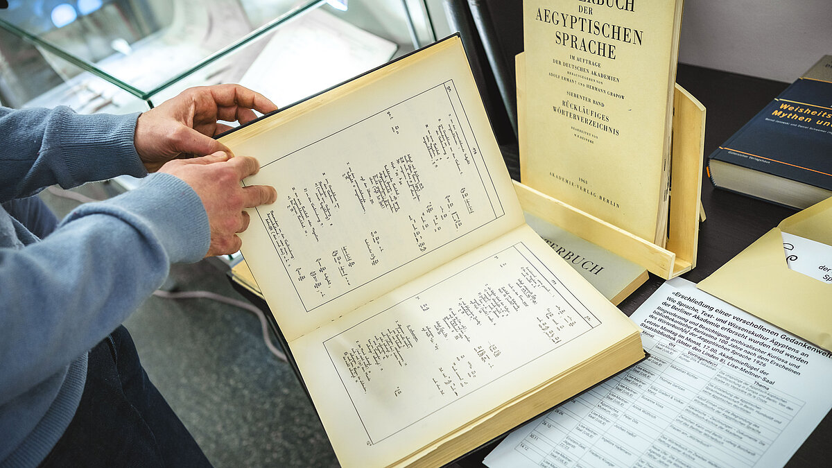 Foto von einem Buch auf einem Ausstellungstisch mit aegyptischen Zeichen, das von einer Person durchblättert wird