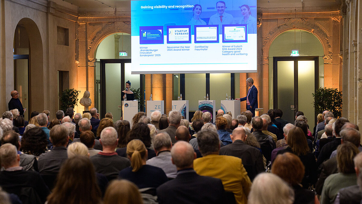 Zwei Personen auf einem Podium im Leibniz-Saal mit der Überschrift "Gaining visibility and recognition" 