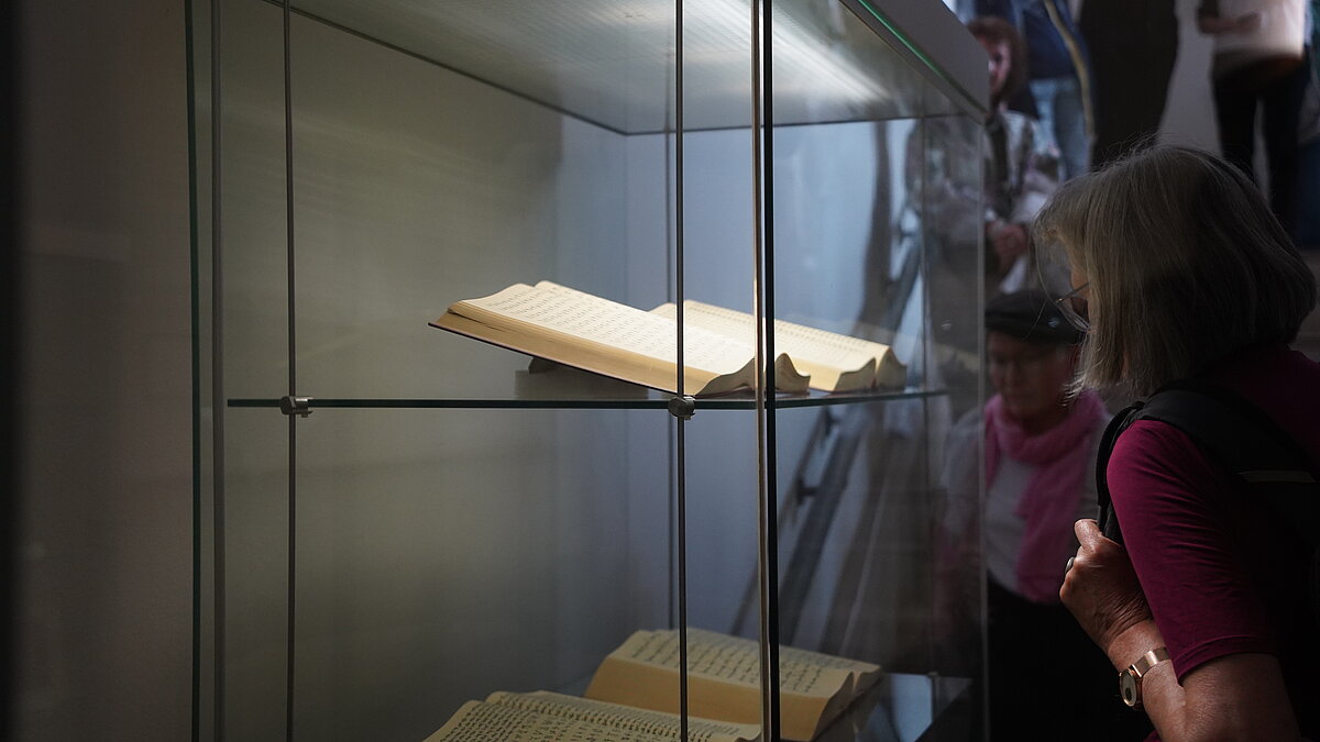 Eine Gruppe von Menschen schaut in eine beleuchtete Glasvitrine, die Bücher ausstellt