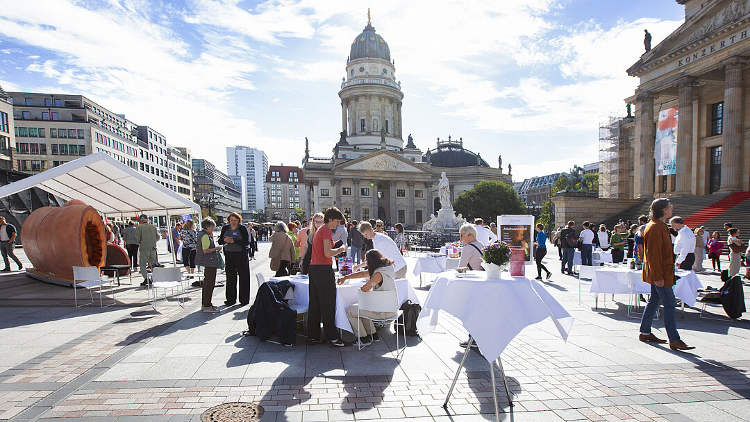 Gendarmenmarkt in der Sonne, auf dem Platz stehen viele weiß gedeckten Tische und ein übergroßes Model einer Arterie, viele Menschen sammeln sich um die Tische und sprechen miteinander