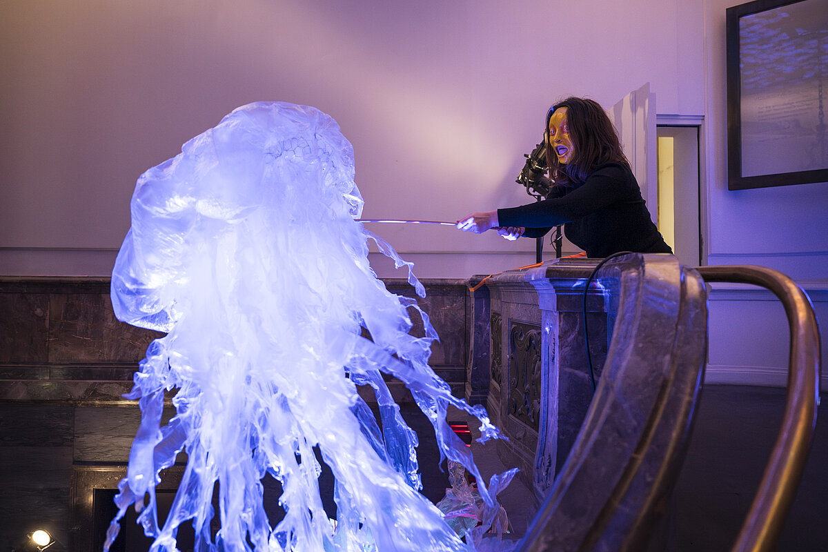 Maskierte Person mit Quallenpuppe im Treppenhaus vor dem Leibniz-Saal