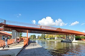 Fußgänger- und Radwegbrücke Passerelle Lucie-Bréard in Saint-Denis, Frankreich: eine markante, rot-orange gestrichene Stahlbrücke über einen Kanal, mit Promenade auf Wasserniveau und erhöhtem Brückendeck, belebt von Passanten und einem E-Roller-Fahrer, vor blauem Herbsthimmel.