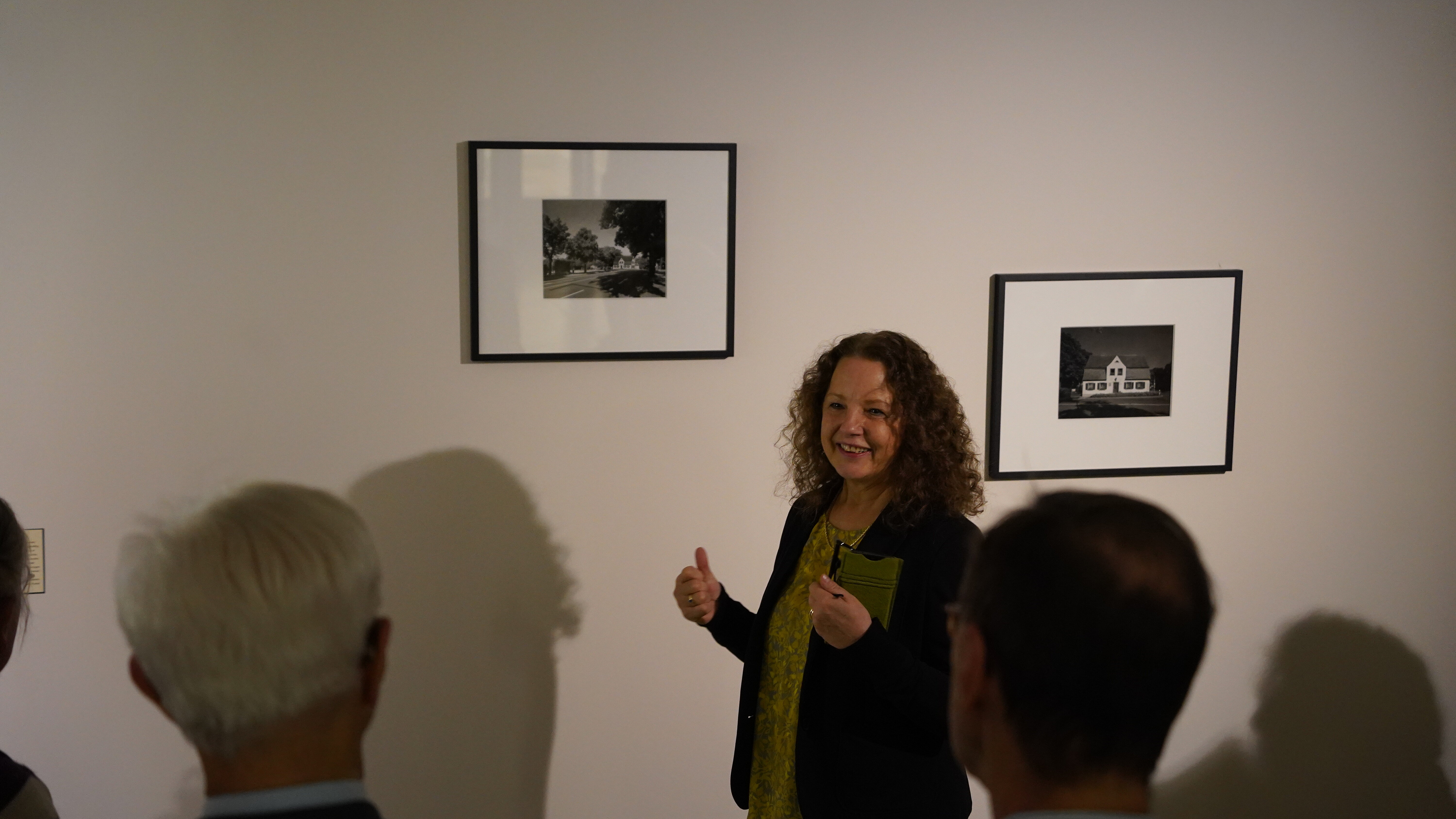 Angela Steinsiek steht vor zwei gerahmten Bildern und erklärt ihren Zuhörer:innen die Ausstellung