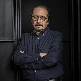 Porträt von Pablo A. Marquet mit verschränkten Armen, dunkelblauem Hemd und dunklem Hintergrund mit Paneelen.