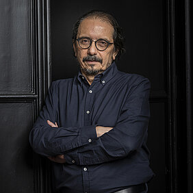 Porträt von Pablo A. Marquet mit verschränkten Armen, dunkelblauem Hemd und dunklem Hintergrund mit Paneelen.