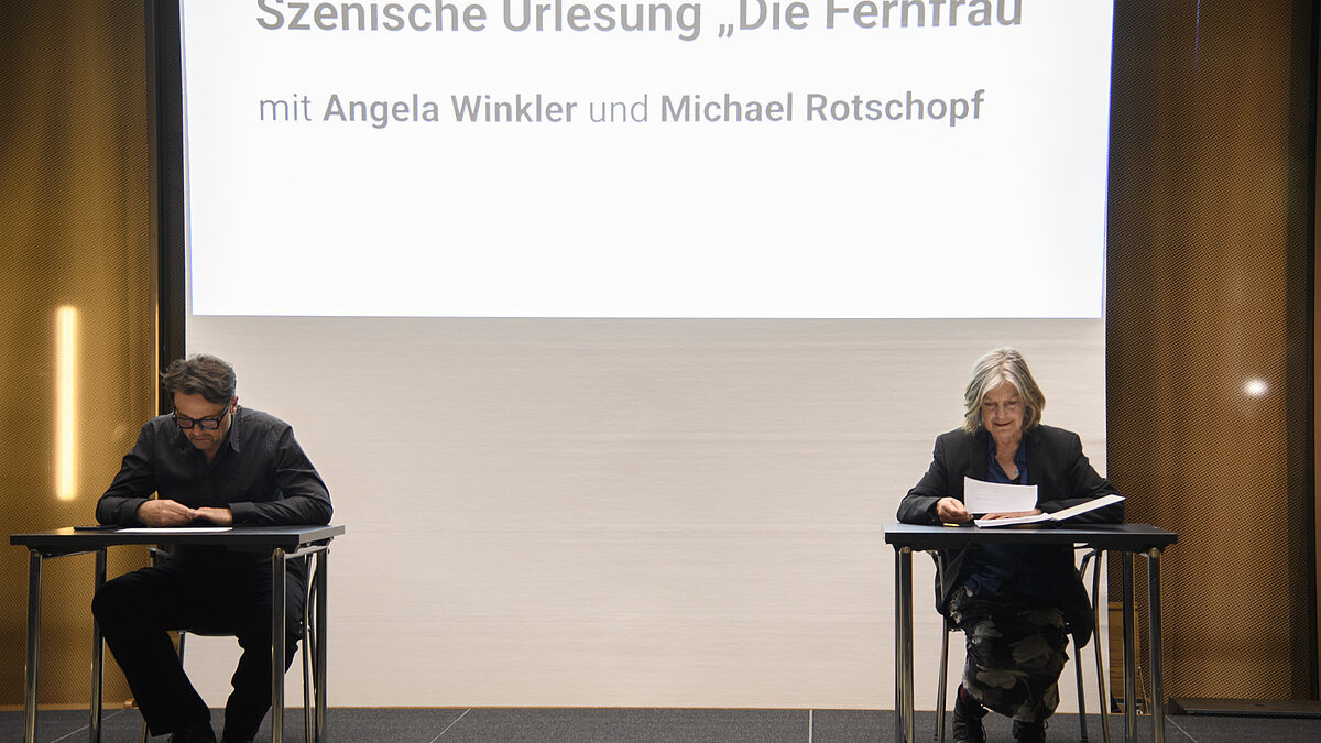 Auf einer Bühne wird ein Theaterstück von zwei Personen vorgelesen. 