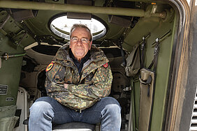 Boris Pistorius posiert mit verschränkten Armen in einem Militärpanzer. Er trägt Jeans und eine Camouflage Jacke