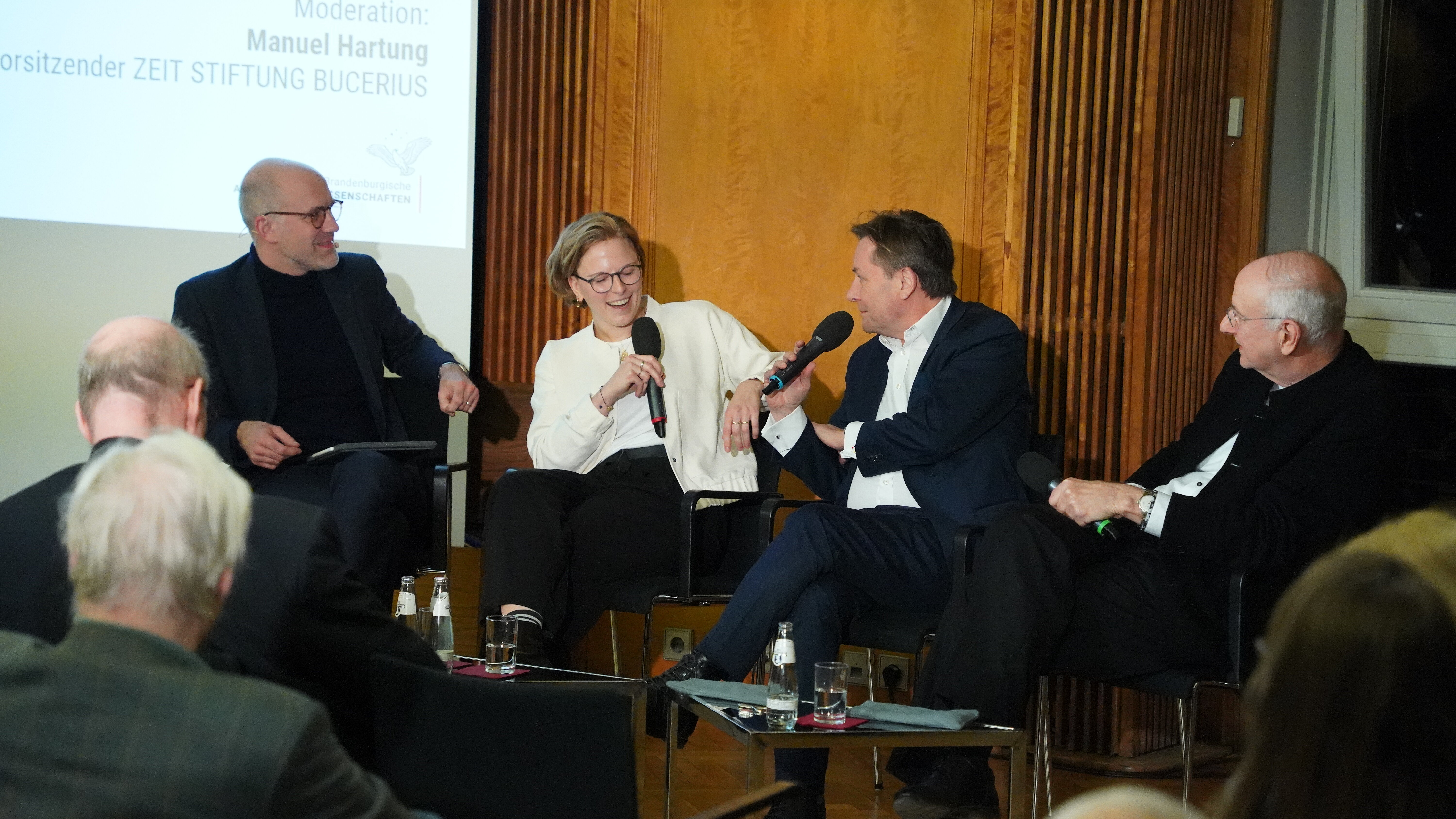 Vier Personen sitzen im Panel, halten Mikrofone und lachen