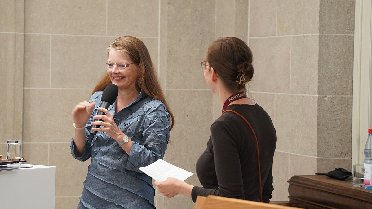 Dagmar Schäfer spricht im Foyer des Akademiegebäudes in ein Mikrophon und lacht. Marianne Seidig hört gespannt zu